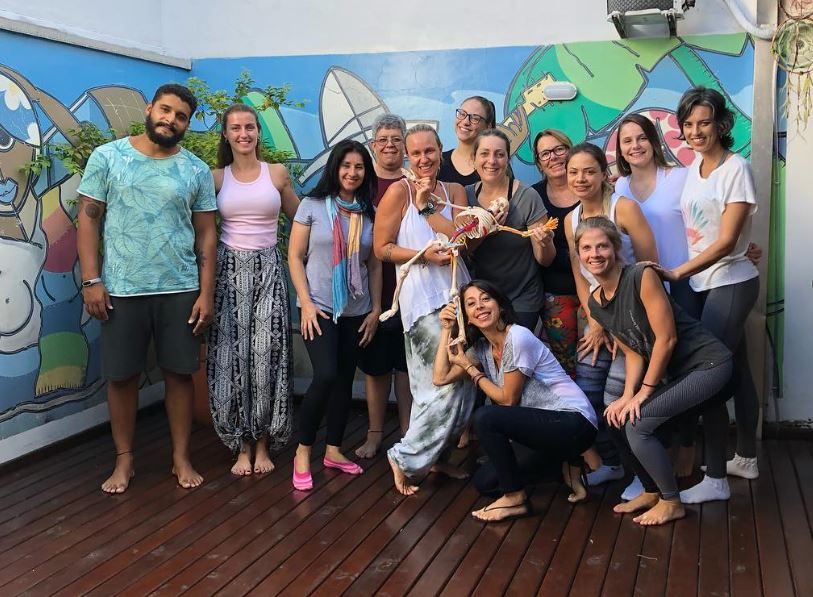 Turma da formação reunida em frente a um mural colorido, segurando um esqueleto de estudo de anatomia
